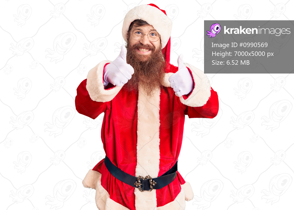 Handsome young red head man with long beard wearing santa claus costume approving doing positive gesture with hand, thumbs up smiling and happy for success. winner gesture. 