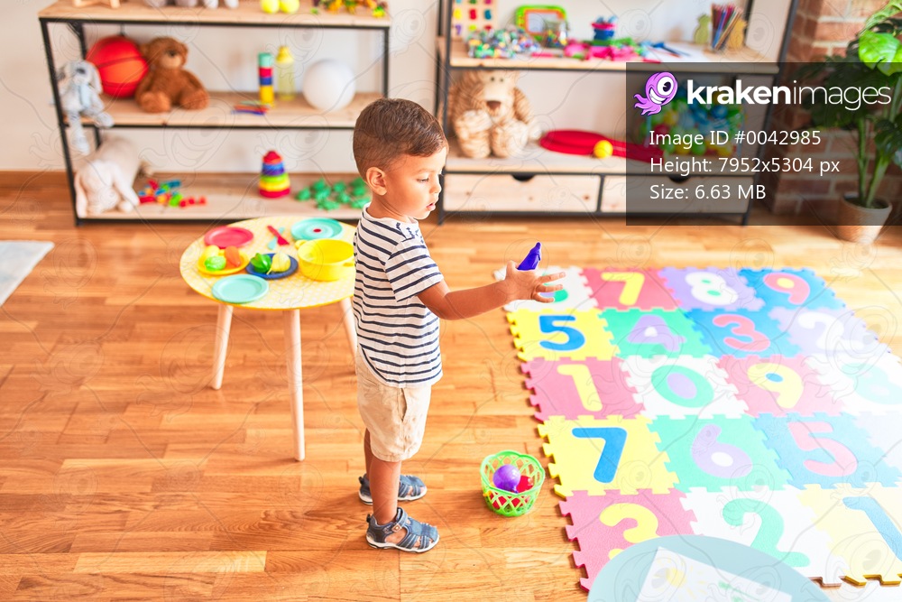 Beautiful toddler boy playing meals with plastic plates, fruits and vegetables at kindergarten