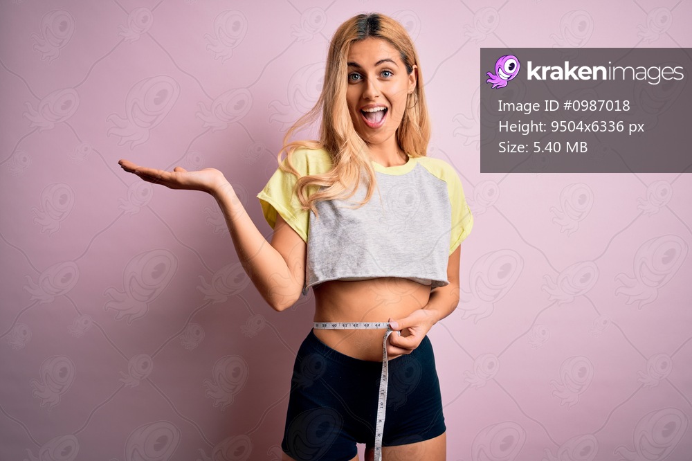 Young beautiful blonde slim woman doing sport using tape measure controlling weight very happy and excited, winner expression celebrating victory screaming with big smile and raised hands