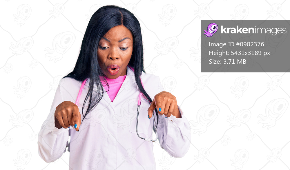 Young african american woman wearing doctor stethoscope pointing down with fingers showing advertisement, surprised face and open mouth 