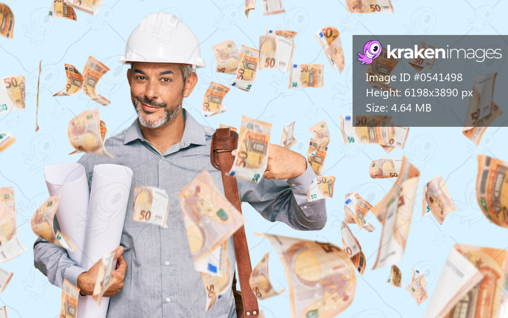 Middle age grey-haired man wearing safety helmet holding blueprints pointing finger to one self smiling happy and proud