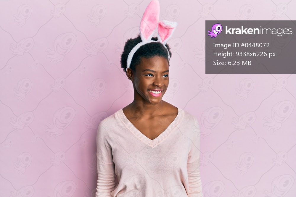 Young african american girl wearing cute easter bunny ears looking away to side with smile on face, natural expression. laughing confident. 