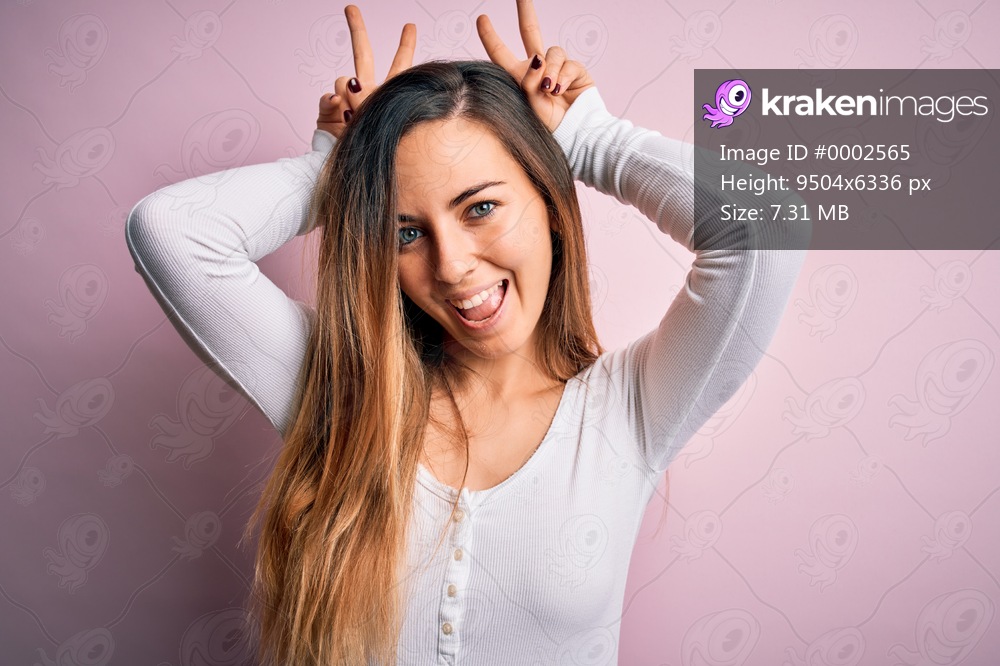 Young beautiful blonde woman with blue eyes wearing white t-shirt over pink background Posing funny and crazy with fingers on head as bunny ears, smiling cheerful