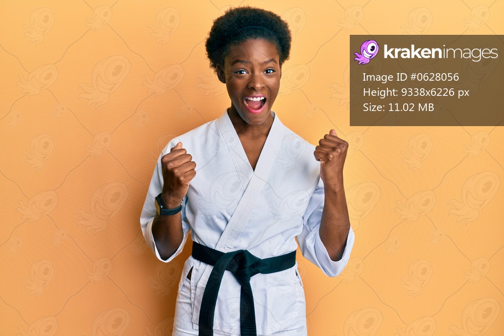 Young african american girl wearing karate kimono and black belt celebrating surprised and amazed for success with arms raised and open eyes. winner concept. 