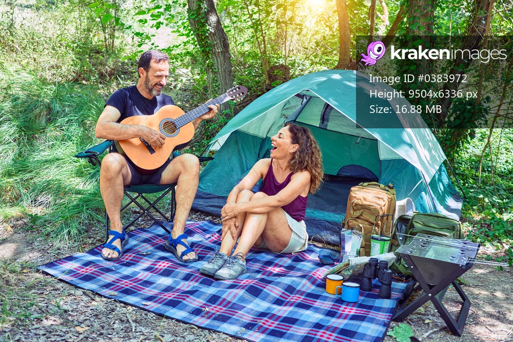 Middle age couple  of hiker smiling happy camping at the forest. Sitting on the floor singing song playing classical guitar