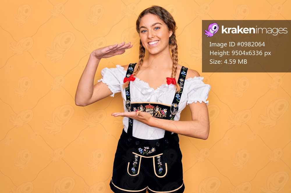 Young beautiful blonde german woman with blue eyes wearing traditional octoberfest dress gesturing with hands showing big and large size sign, measure symbol. Smiling looking at the camera. Measuring concept.