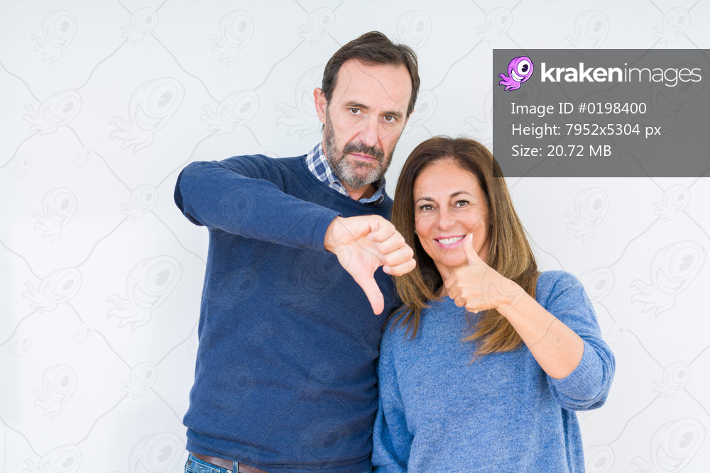 Beautiful middle age couple in love over isolated background Doing thumbs up and down, disagreement and agreement expression. Crazy conflict