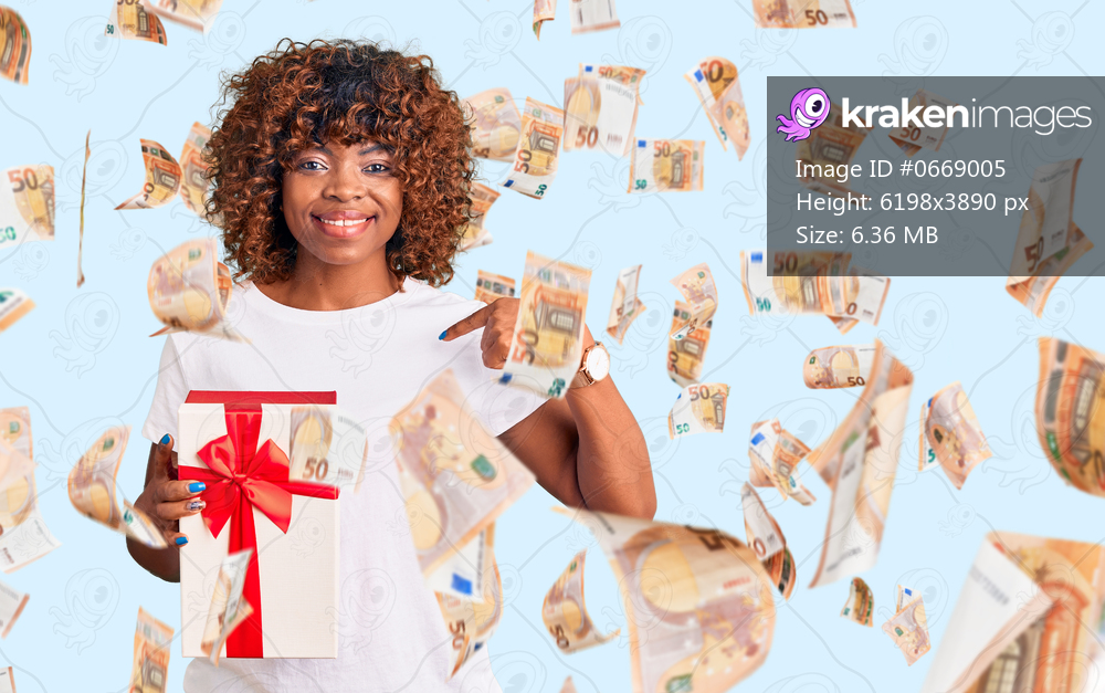 Young african american woman holding gift pointing finger to one self smiling happy and proud