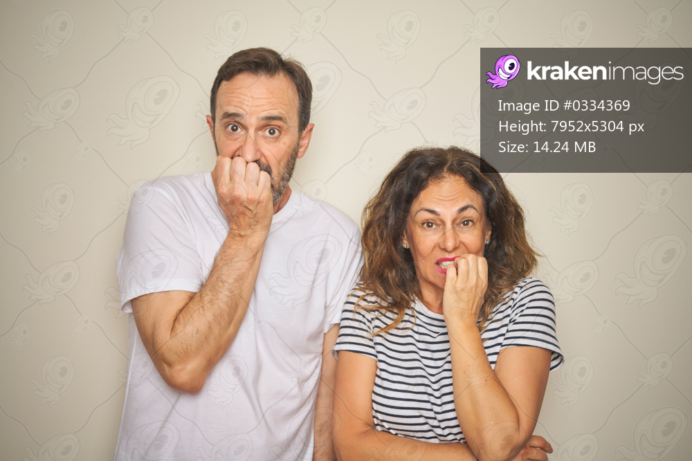 Beautiful middle age couple together standing over isolated white background looking stressed and nervous with hands on mouth biting nails. Anxiety problem.