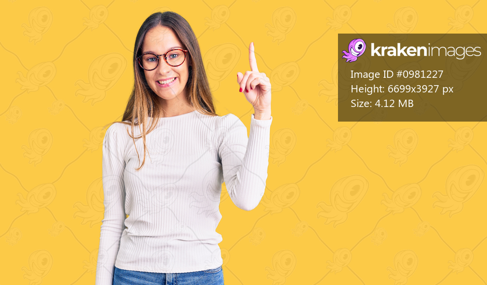 Beautiful brunette young woman wearing casual white sweater and glasses pointing finger up with successful idea. exited and happy. number one. 