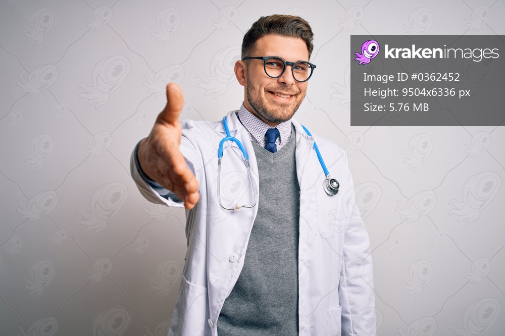 Young doctor man with blue eyes wearing medical coat and stethoscope over isolated background smiling friendly offering handshake as greeting and welcoming. Successful business.