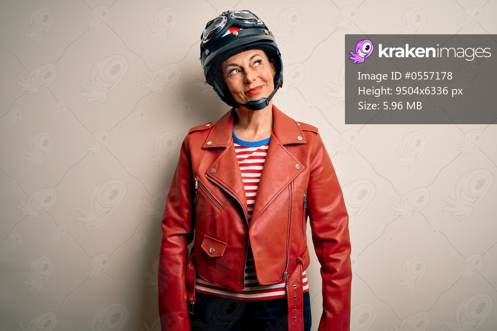 Middle age motorcyclist woman wearing motorcycle helmet and jacket over white background smiling looking to the side and staring away thinking.