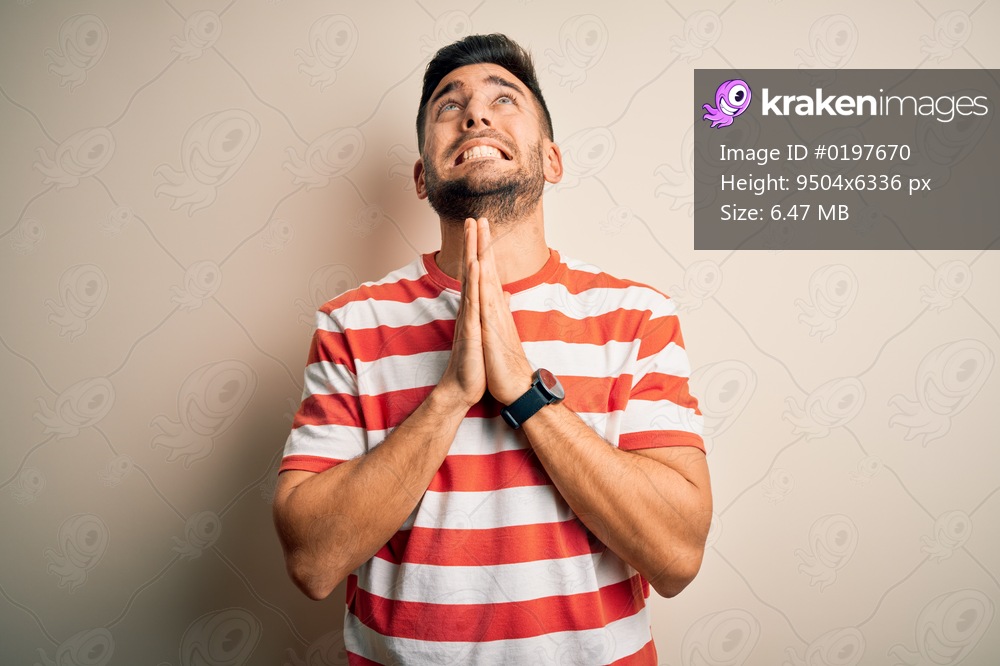 Young handsome man wearing casual striped t-shirt standing over isolated white background begging and praying with hands together with hope expression on face very emotional and worried. Begging.