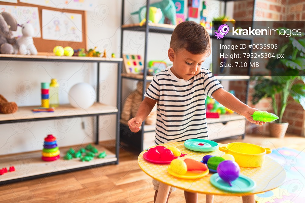 Beautiful toddler boy playing meals with plastic plates, fruits and vegetables at kindergarten
