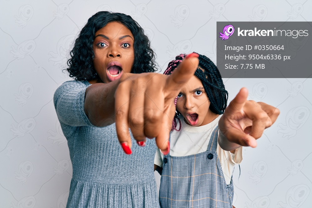 Beautiful african american mother and daughter wearing casual clothes and hugging pointing with finger surprised ahead, open mouth amazed expression, something on the front 