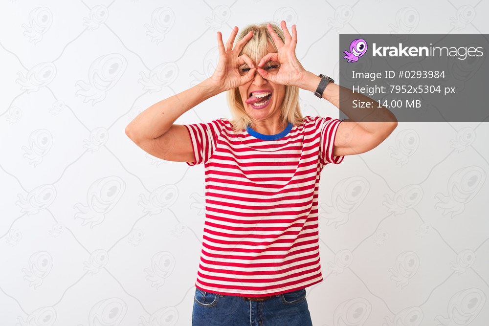 Middle age woman wearing casual striped t-shirt standing over isolated white background doing ok gesture like binoculars sticking tongue out, eyes looking through fingers. Crazy expression.