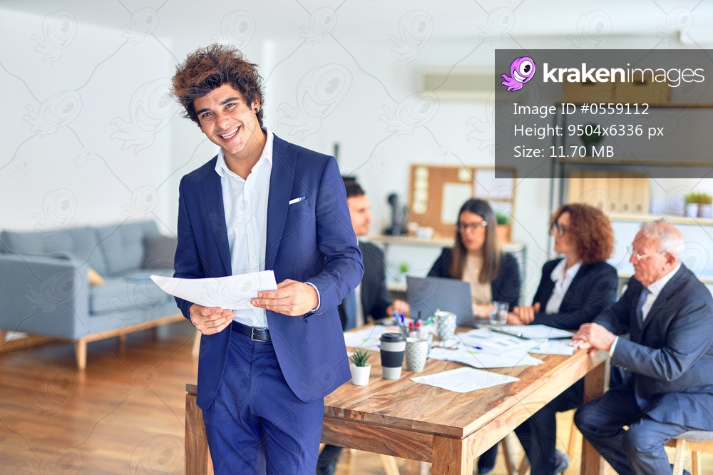 Group of business workers smiling happy and confident working together in a meeting. One of them, standing with smile on face reading documents at the office.