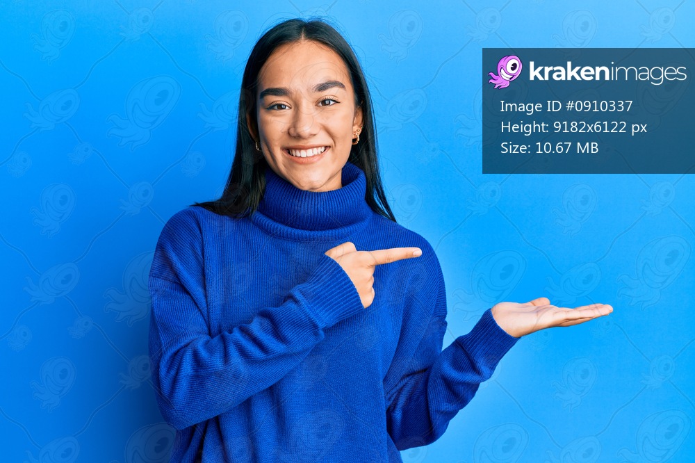 Young asian woman wearing casual winter sweater amazed and smiling to the camera while presenting with hand and pointing with finger. 
