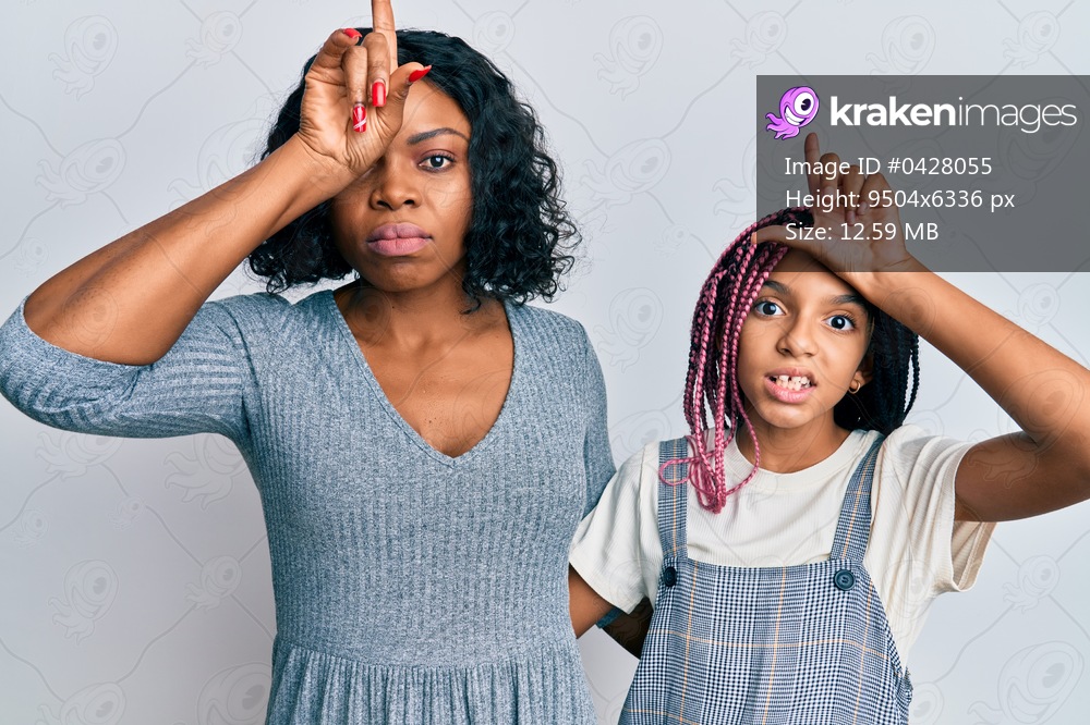 Beautiful african american mother and daughter wearing casual clothes and hugging making fun of people with fingers on forehead doing loser gesture mocking and insulting. 