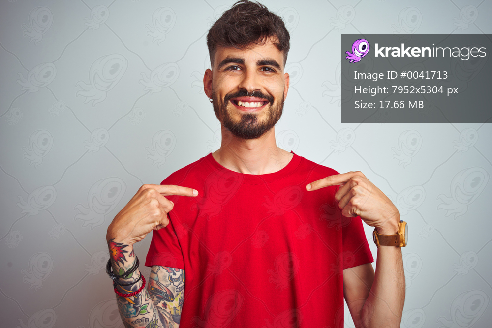 Young man with tattoo wearing red t-shirt standing over isolated white background looking confident with smile on face, pointing oneself with fingers proud and happy.