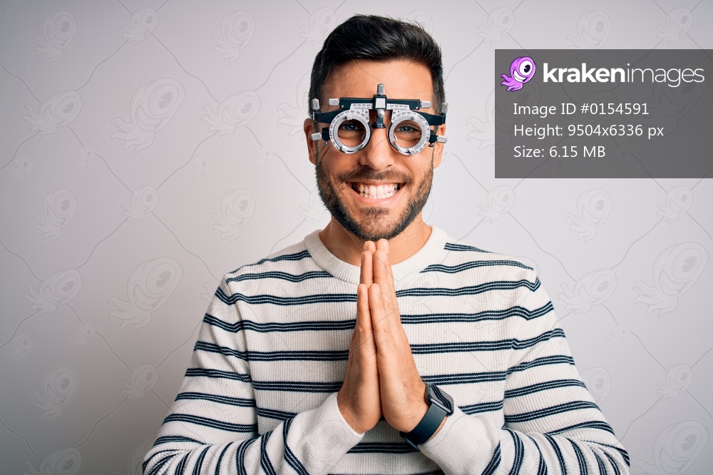 Young handsome man with beard wearing optometry glasses over isolated white background praying with hands together asking for forgiveness smiling confident.