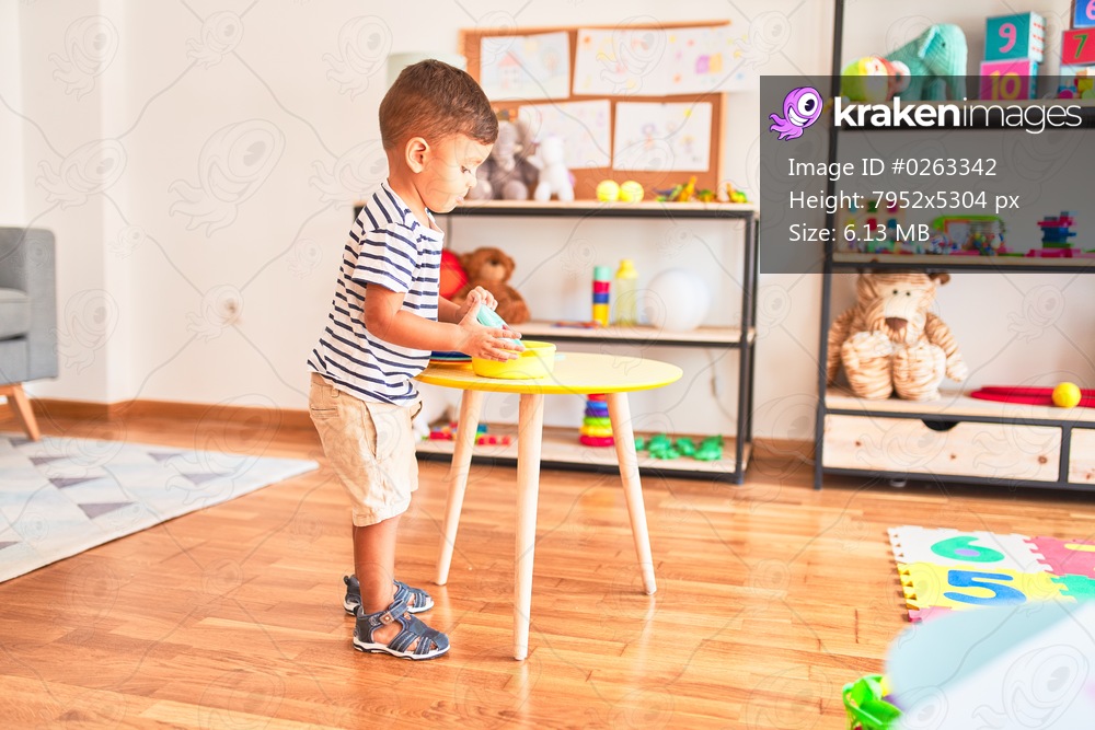 Beautiful toddler boy playing meals with plastic plates, fruits and vegetables at kindergarten