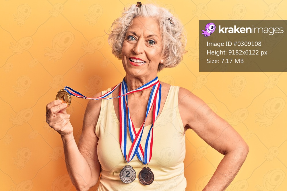 Senior grey-haired woman wearing medals looking positive and happy standing and smiling with a confident smile showing teeth 