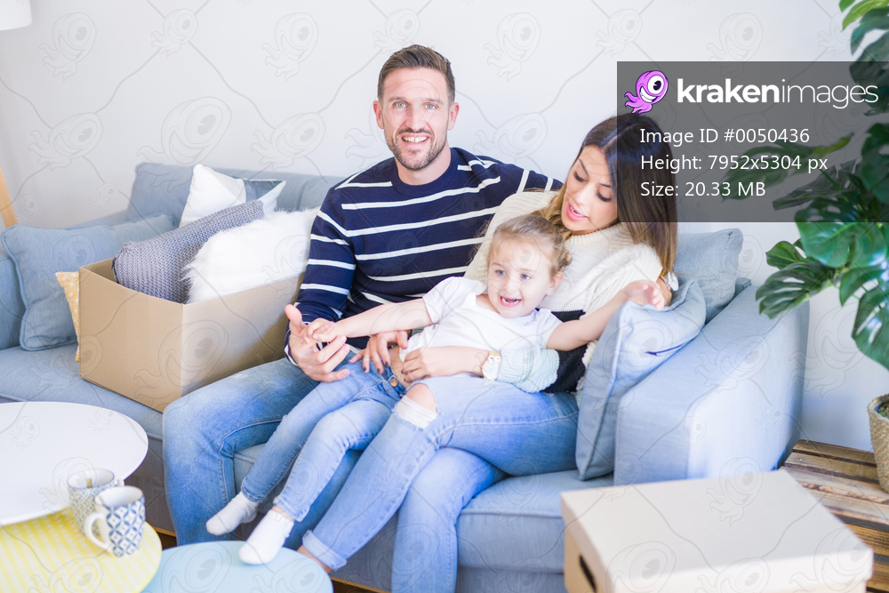 Beautiful family, parents sitting on the sofa drinking coffee looking his kid playing at new home around cardboard boxes
