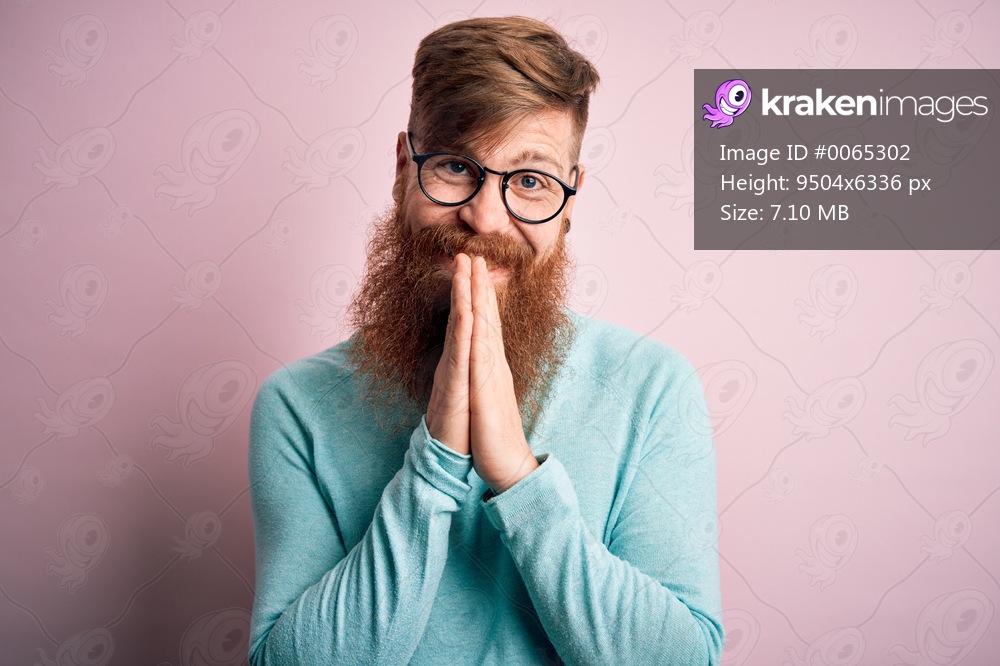 Handsome Irish redhead man with beard wearing glasses over pink isolated background praying with hands together asking for forgiveness smiling confident.