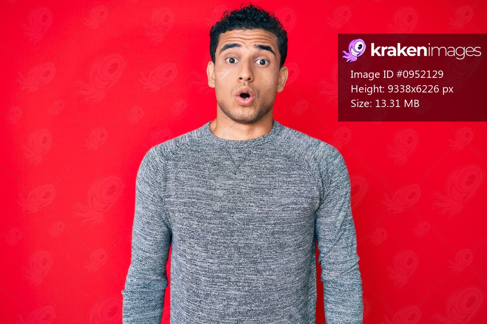 Young handsome hispanic man over red background scared and amazed with open mouth for surprise, disbelief face 