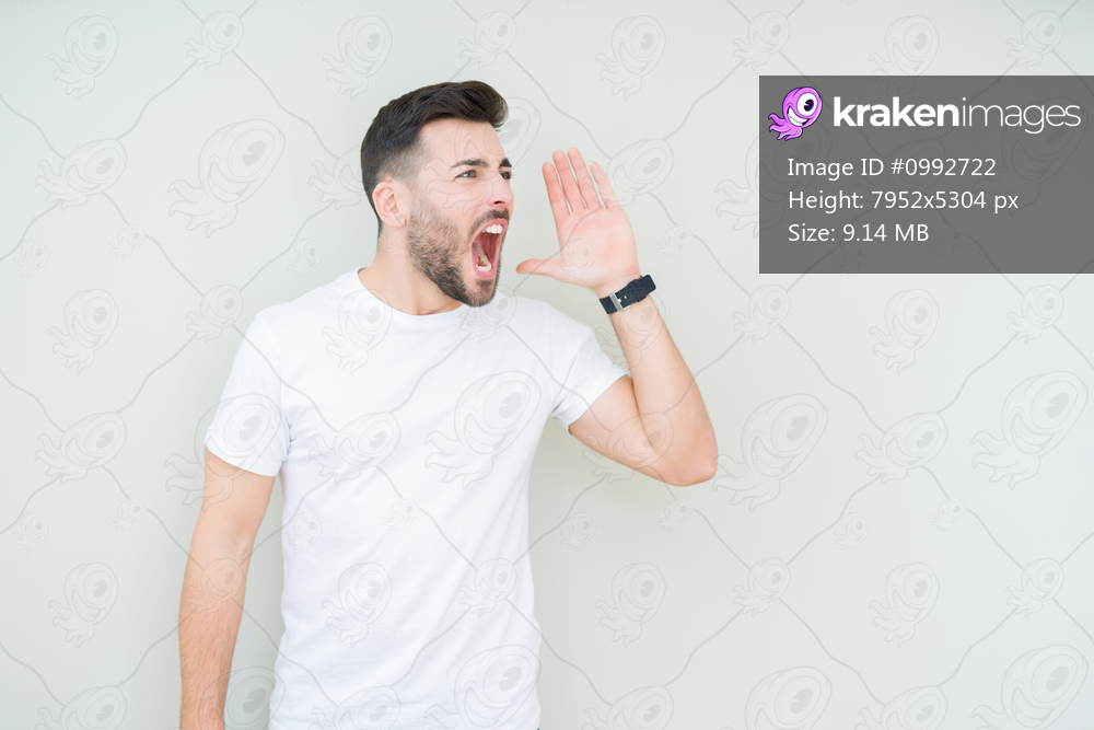 Young handsome man wearing casual white t-shirt over isolated background shouting and screaming loud to side with hand on mouth. Communication concept.