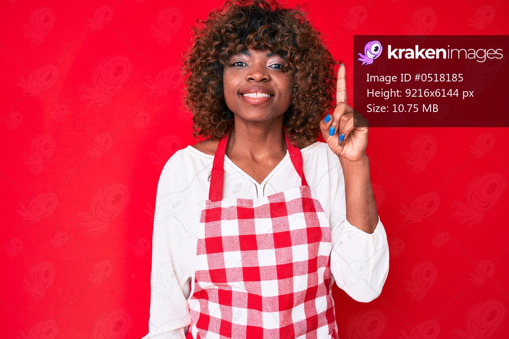 Young african american woman wearing apron smiling with an idea or question pointing finger up with happy face, number one 