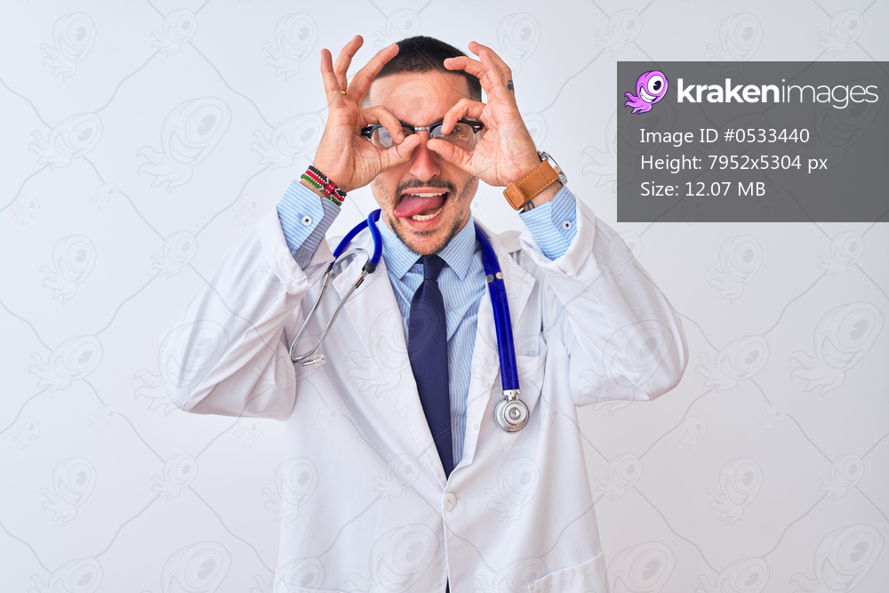 Young doctor man wearing stethoscope over isolated background doing ok gesture like binoculars sticking tongue out, eyes looking through fingers. Crazy expression.