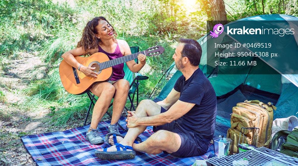 Middle age couple  of hiker smiling happy camping at the forest. Sitting on the floor singing song playing classical guitar